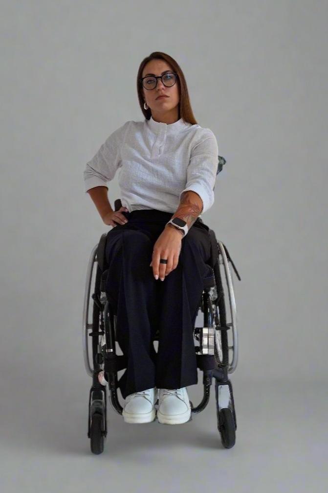 A woman in a wheelchair looking straight forward, she is dressed in adaptive office clothing made by Vilber's