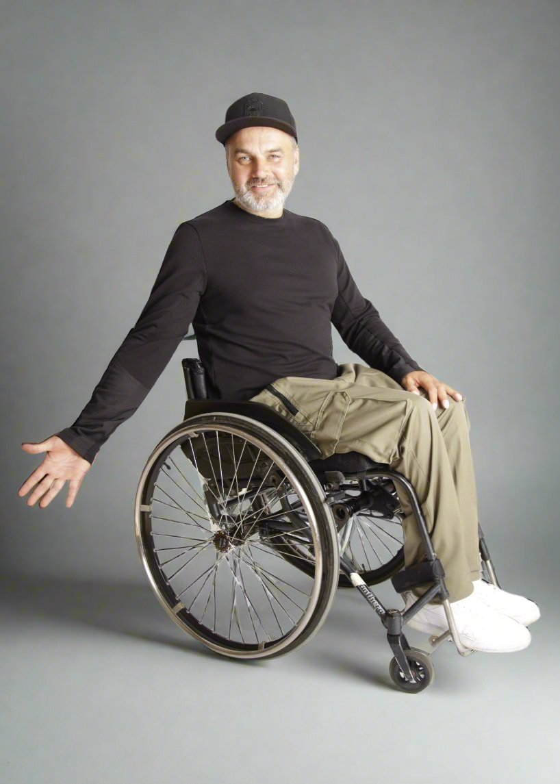 A man sitting in a wheelchair wearing Vilber's black long sleeve shirt and wheelchair adaptive trousers